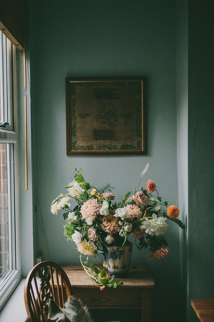 flowers in a vase sitting on a table next to a chair with a cat laying beside it