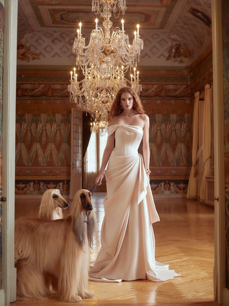 a woman standing next to two dogs in a room with chandelier hanging from the ceiling