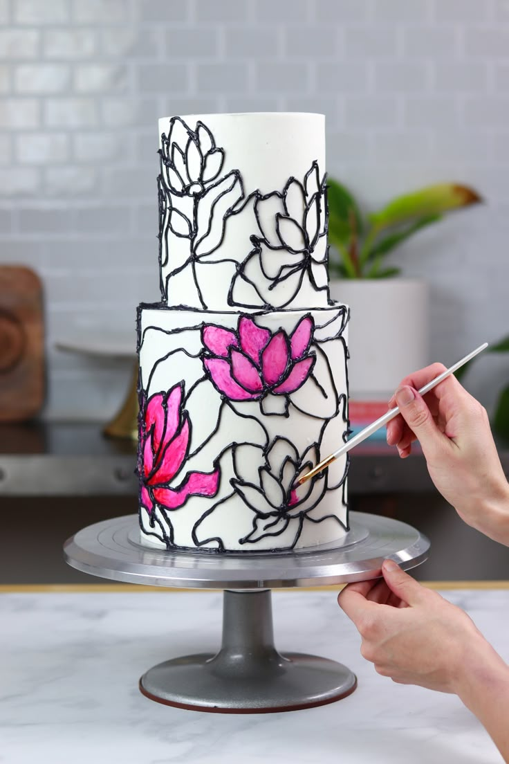 a woman is decorating a white and pink cake with flowers on the frosting