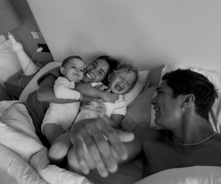 a man laying in bed with two children and an adult holding the baby up to him