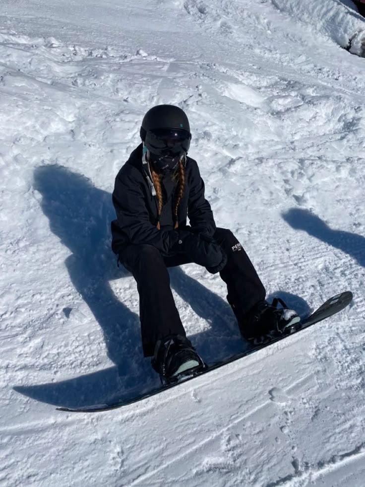 a snowboarder is sitting in the snow with his shadow on the ground behind him