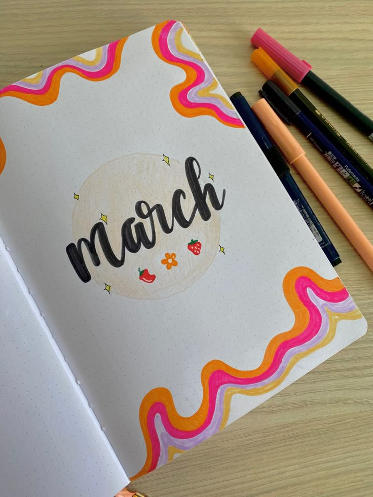 an open notebook with the word march written on it next to some colored pencils