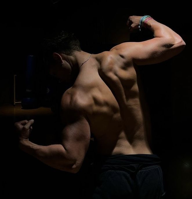 a man with no shirt on is flexing his muscles in the dark while holding onto a bar