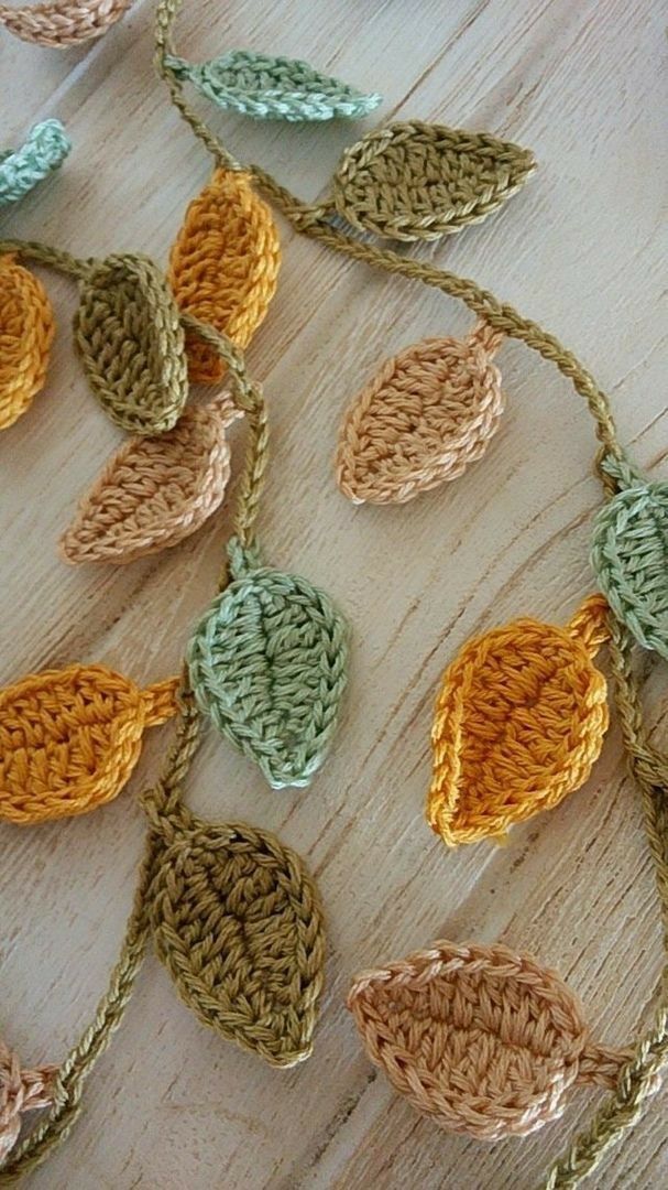 crocheted leaves are hanging on a wooden surface with chains attached to them, all in different colors