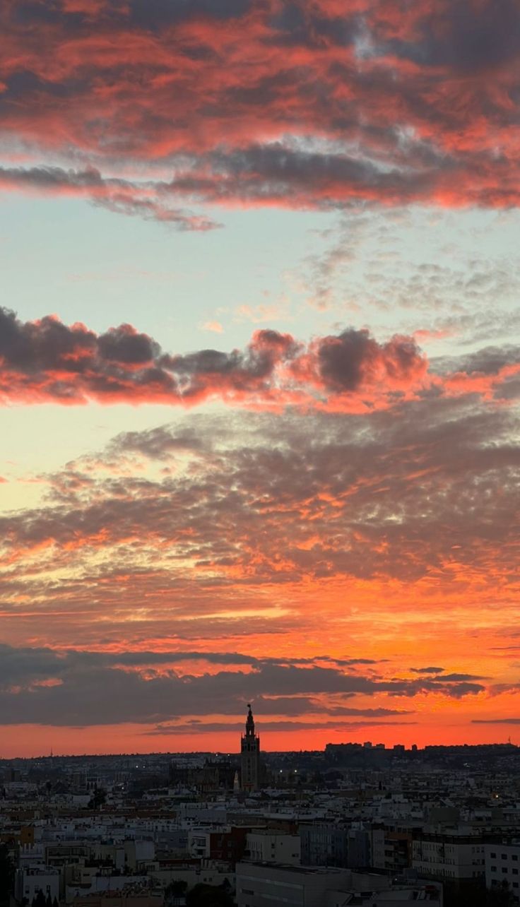 an airplane flying in the sky over a city with buildings and clouds at sunset or dawn