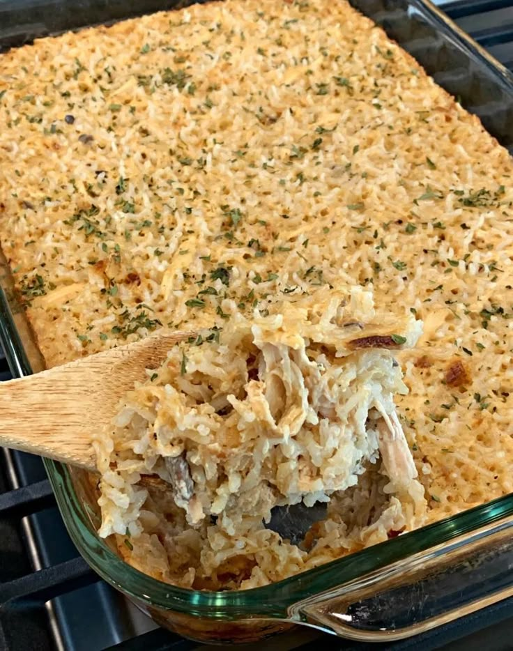 a casserole dish with chicken and rice in it being lifted from the oven by a wooden spoon