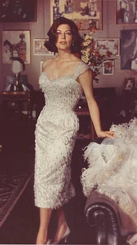 a woman in a white dress is standing next to a couch and some pictures on the wall