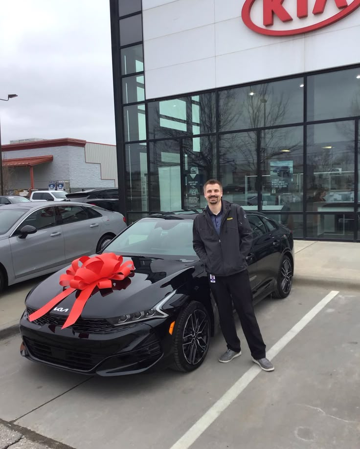 a man standing next to a black car with a red bow on it