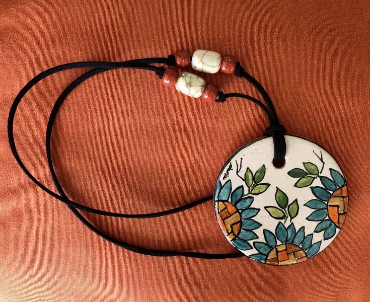 a white and blue flowered ceramic pendant on a black cord with two beaded beads