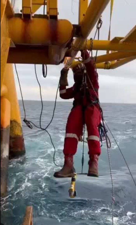 a man in red jumps into the water while holding onto a rope and wearing safety equipment