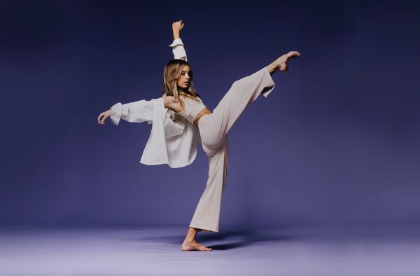 a woman in white is doing a dance pose on a purple background with her arms stretched out