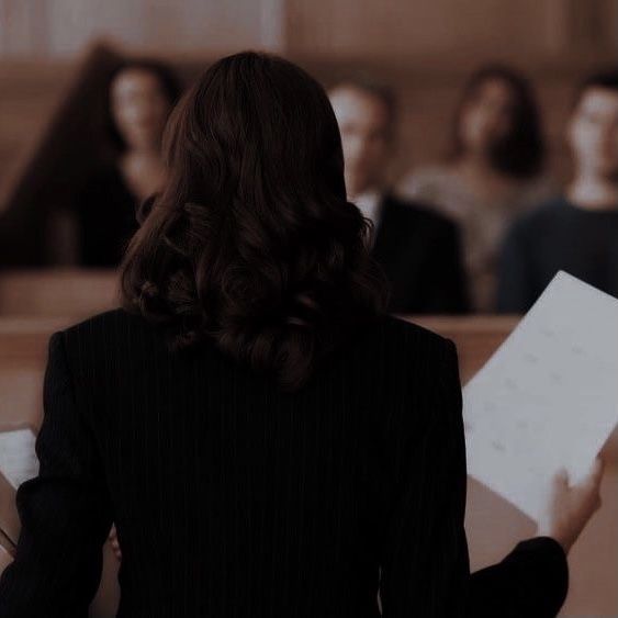 a woman sitting at a table with papers in front of her and other people behind her