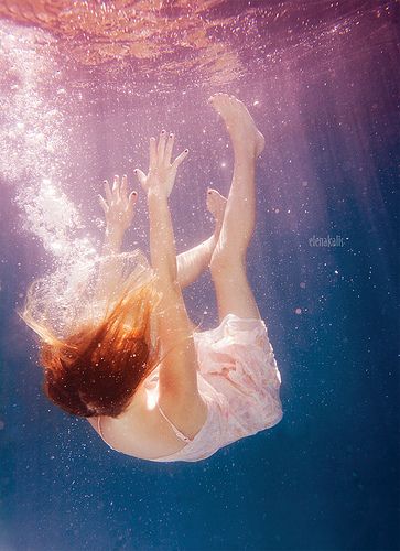 a woman in a white dress under water with her hands up above the water's surface