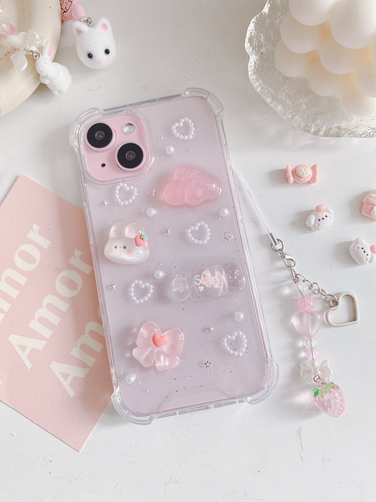 an iphone case with various charms on it and a pink card next to the phone