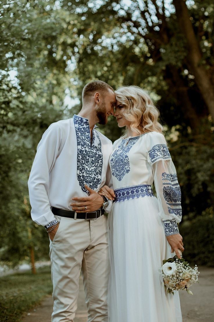 a man and woman standing next to each other on a path in front of trees