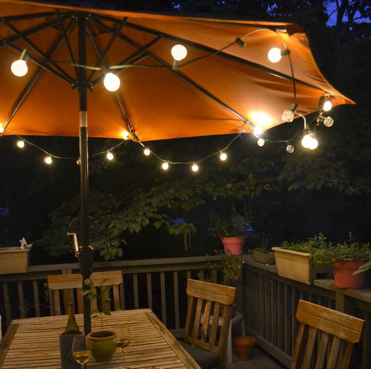 an umbrella is lit up over a table with chairs and potted plants on it