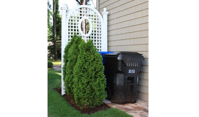 a white trellis next to a black trash can on the side of a house