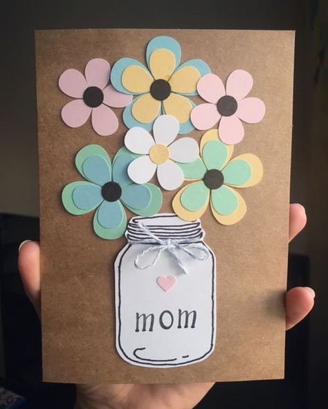 a person holding up a card with flowers in a mason jar