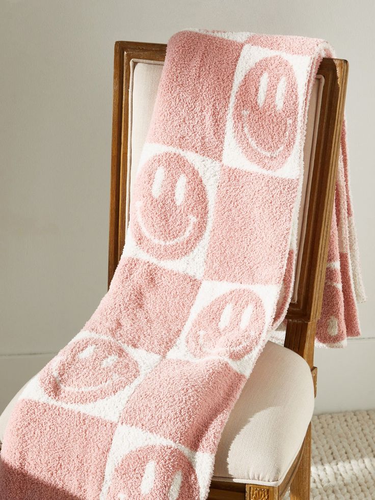 a pink towel with smiley faces on it sitting on a chair in front of a white wall