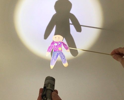 a person holding a microphone with a shadow on the wall behind them that has a small doll hanging from it