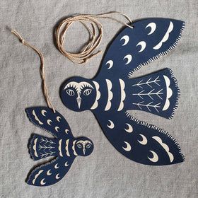 two blue and white fish shaped ornaments on a gray cloth with twine cord in the middle