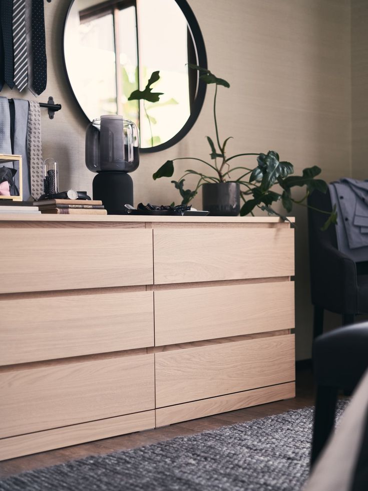 a bedroom with a dresser, mirror and plants on it's sideboard in front of the bed