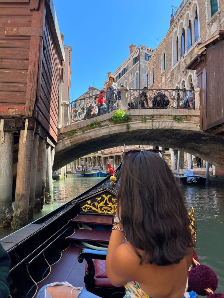 a woman sitting on the back of a boat under a bridge in venice, italy