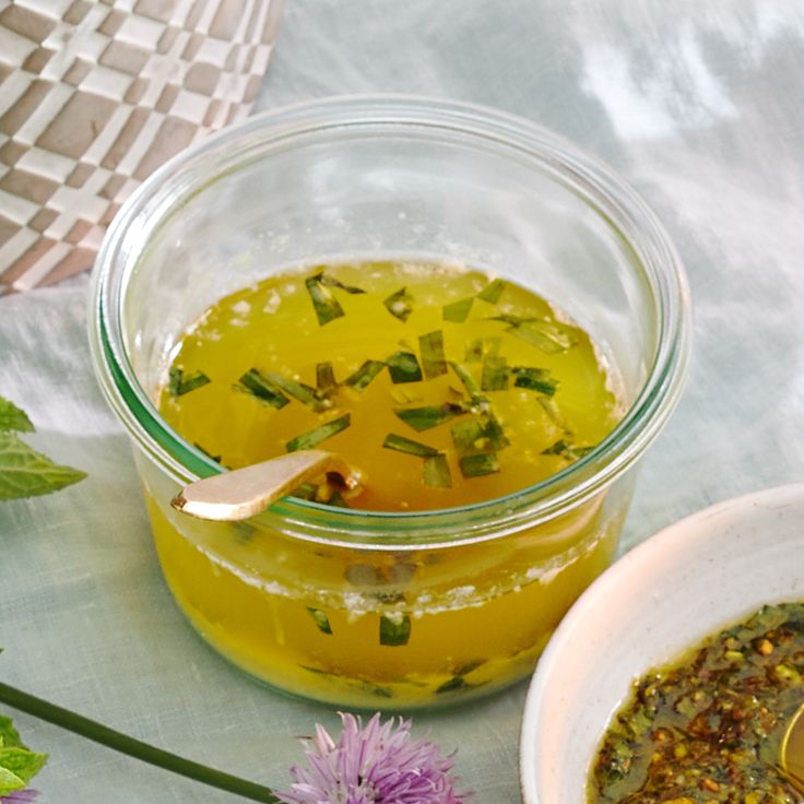 a glass jar filled with green liquid next to a white bowl full of yellow liquid