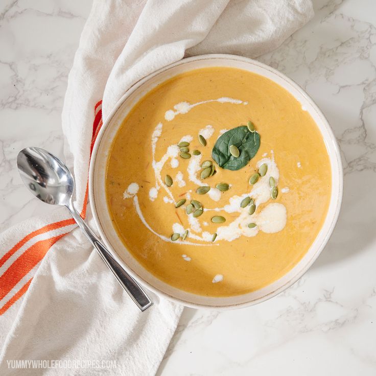 a bowl of carrot soup on a marble counter top with a spoon and napkin next to it