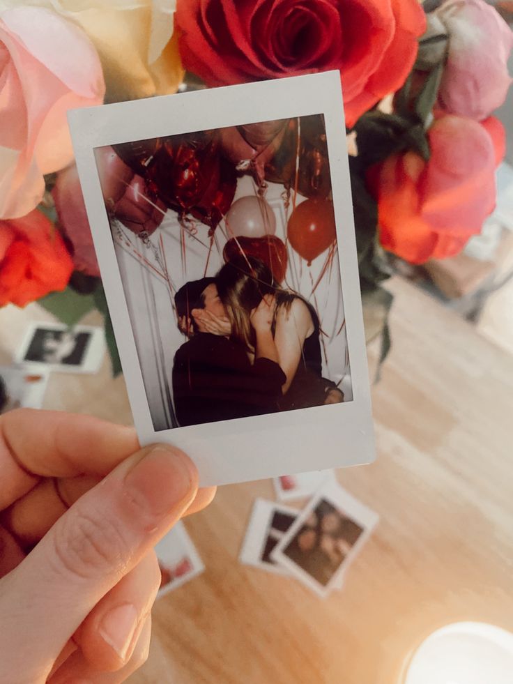 a person holding up a polaroid photo with balloons and flowers in the back ground