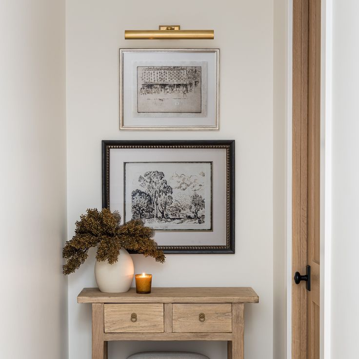 a wooden table topped with a white vase filled with flowers next to a framed picture