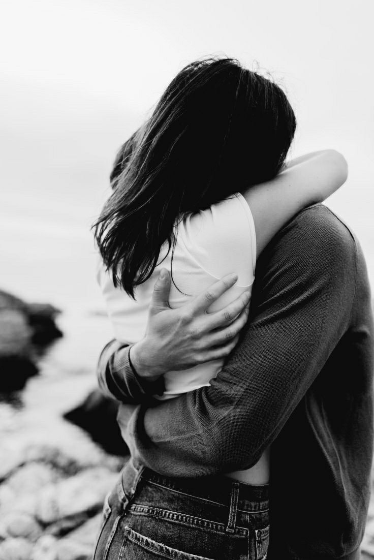 two people embracing each other near the ocean