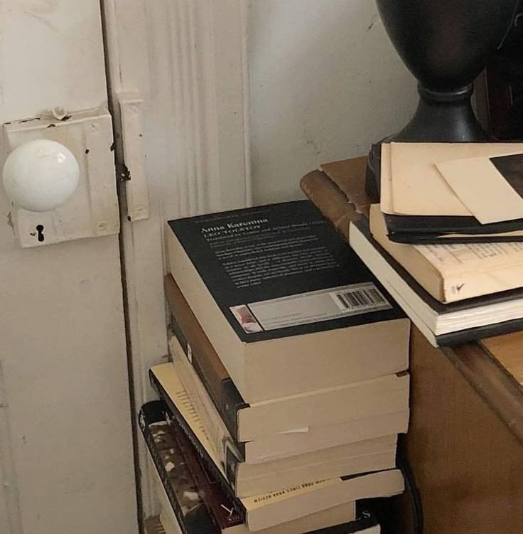 a stack of books sitting on top of a wooden table next to a black lamp