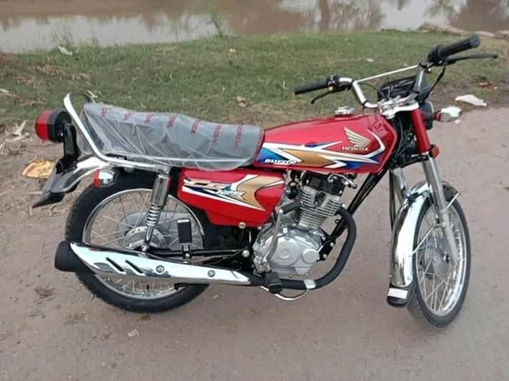 a red and black motorcycle parked on the side of a road next to a body of water