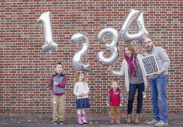 a group of people standing in front of a brick wall holding up large silver balloons