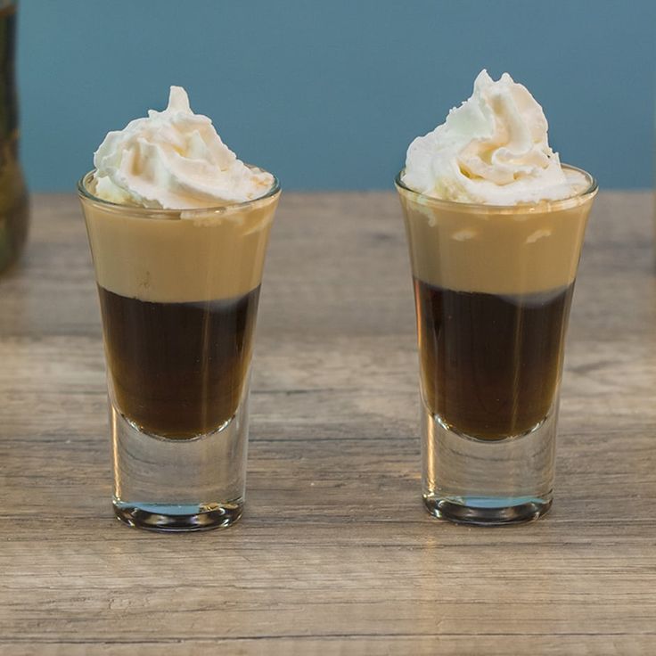 two shot glasses filled with whipped cream on top of a wooden table