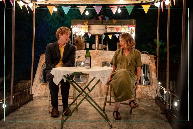 a man and woman sitting at a table in front of a tent with bunting