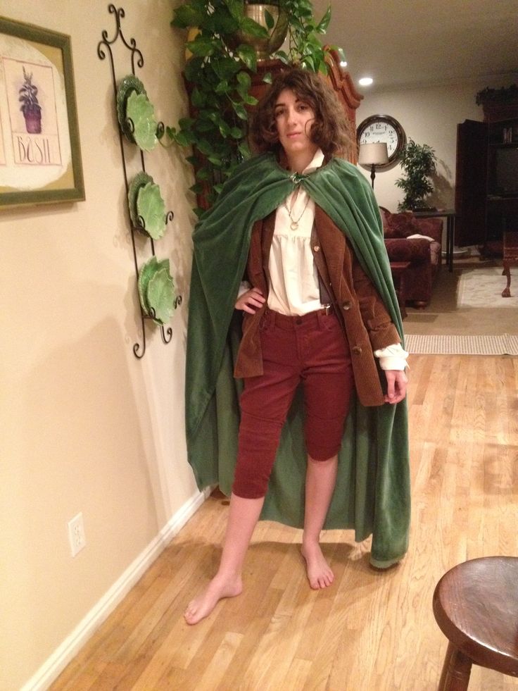 a woman standing in a living room wearing a green cape and red pants with her hands on her hips