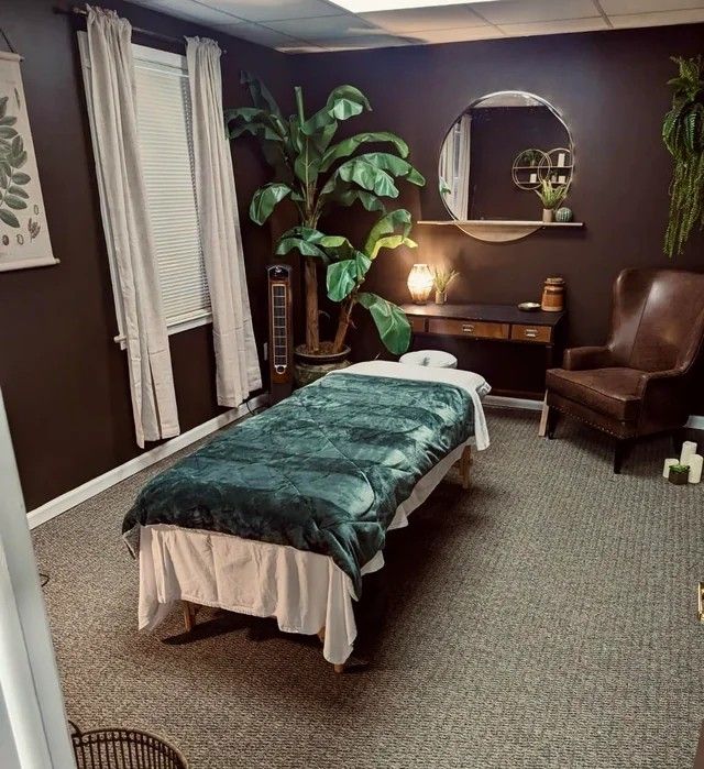 a massage room with a bed, chair and potted plant on the side wall