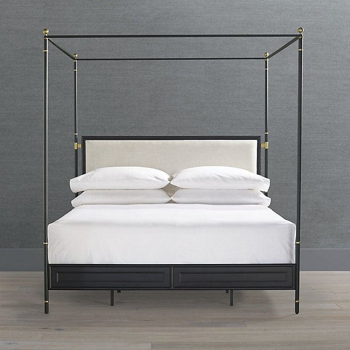 an iron bed frame with white sheets and pillows on the bottom, against a gray wall