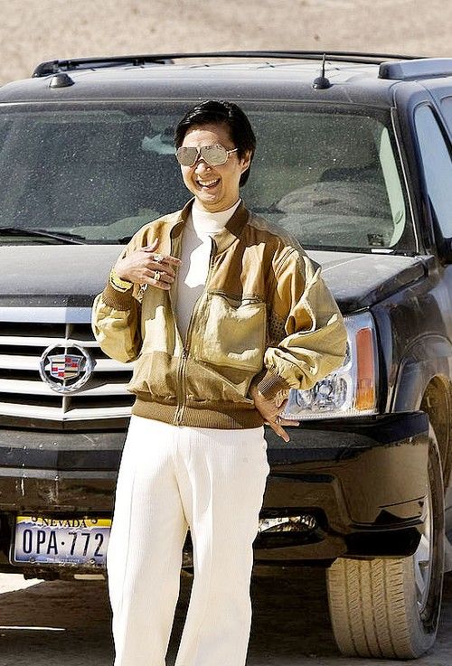 a man standing in front of a black suv with sunglasses on his head and wearing white pants