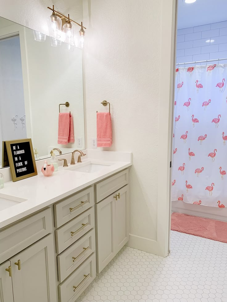 a white bathroom with pink towels hanging on the shower curtain and vanity mirror in front of it