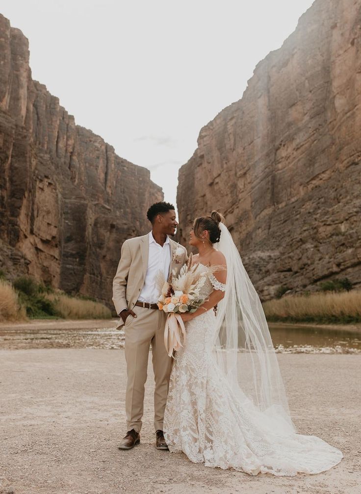 a newly married couple standing in front of some mountains