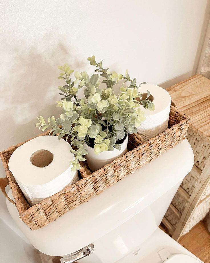 two rolls of toilet paper in a wicker basket on the back of a toilet