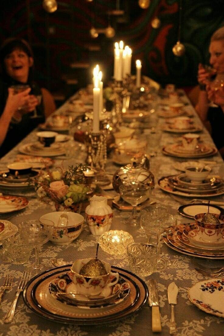 a long table is set with plates and silverware, lit by candlelight candles