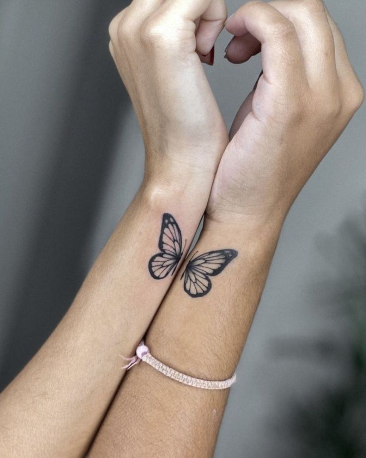 two hands holding each other with butterfly tattoos on their wristbands, one is black and the other is white