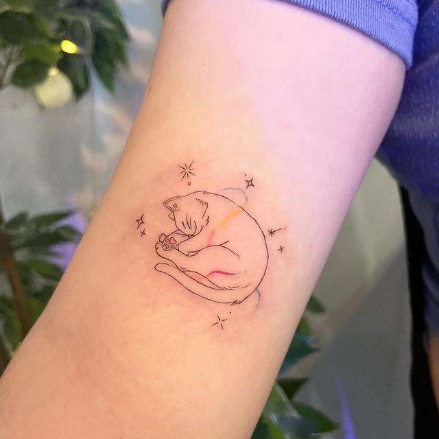 a woman's arm with a small tattoo of a sleeping cat on it and stars in the sky