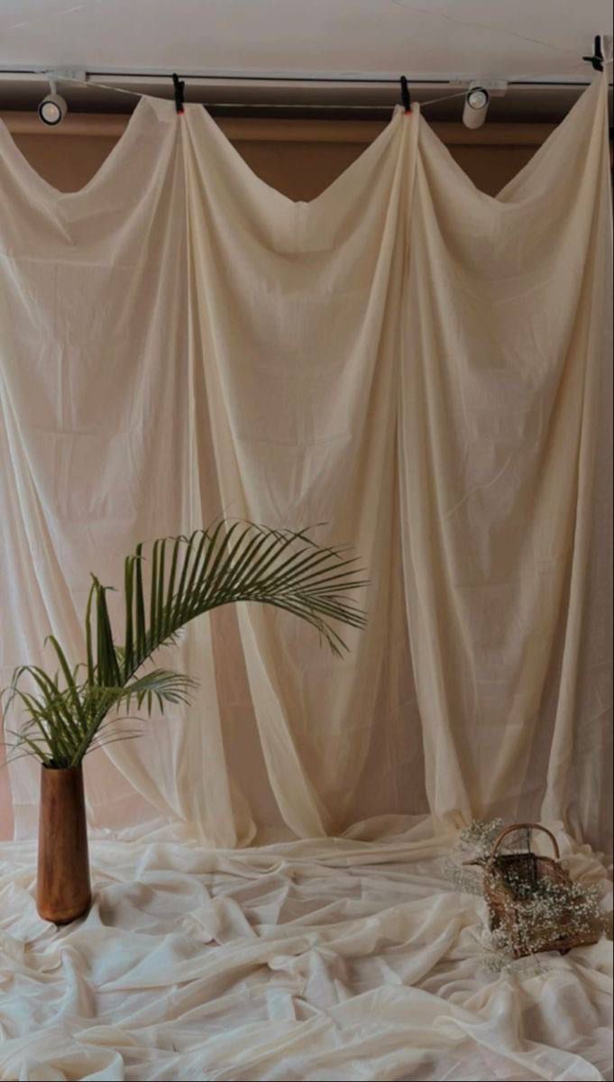 a plant in a vase sitting on top of a bed covered with white sheeting