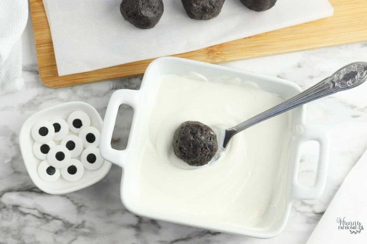 chocolate truffles in a white bowl with cream on the side next to it