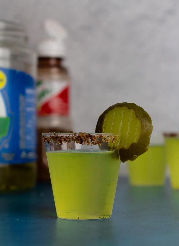 a green drink with a pickle on the rim in front of several other drinks